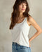 A woman wearing a white tank top and blue jeans.