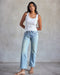 A woman wearing a white ribbed tank top and blue jeans.
