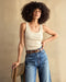 A woman wearing a beige ribbed tank top and blue jeans.
