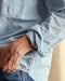 Closeup of a sleeve of a blue chambray utility shirt with chest pockets and button closure, paired with high-waisted blue jeans.