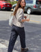 Woman walking on a street holding sunglasses and a tote bag.